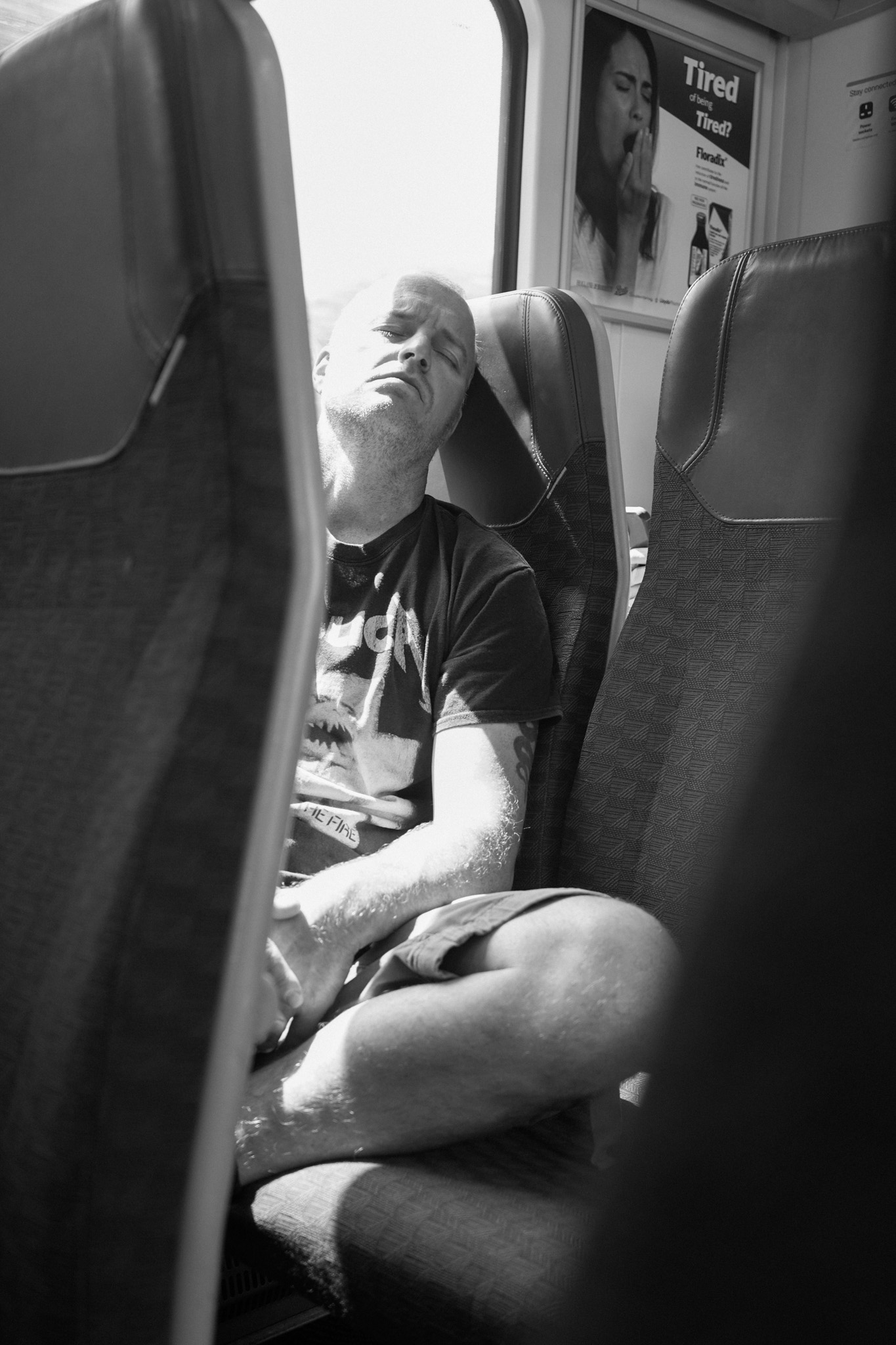 Man slumped asleep on the train beneath an ad reading 'Tired of being tired?'